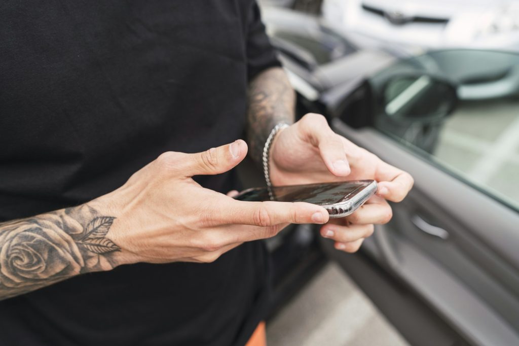 Hands with tattoos holding a phone near the car