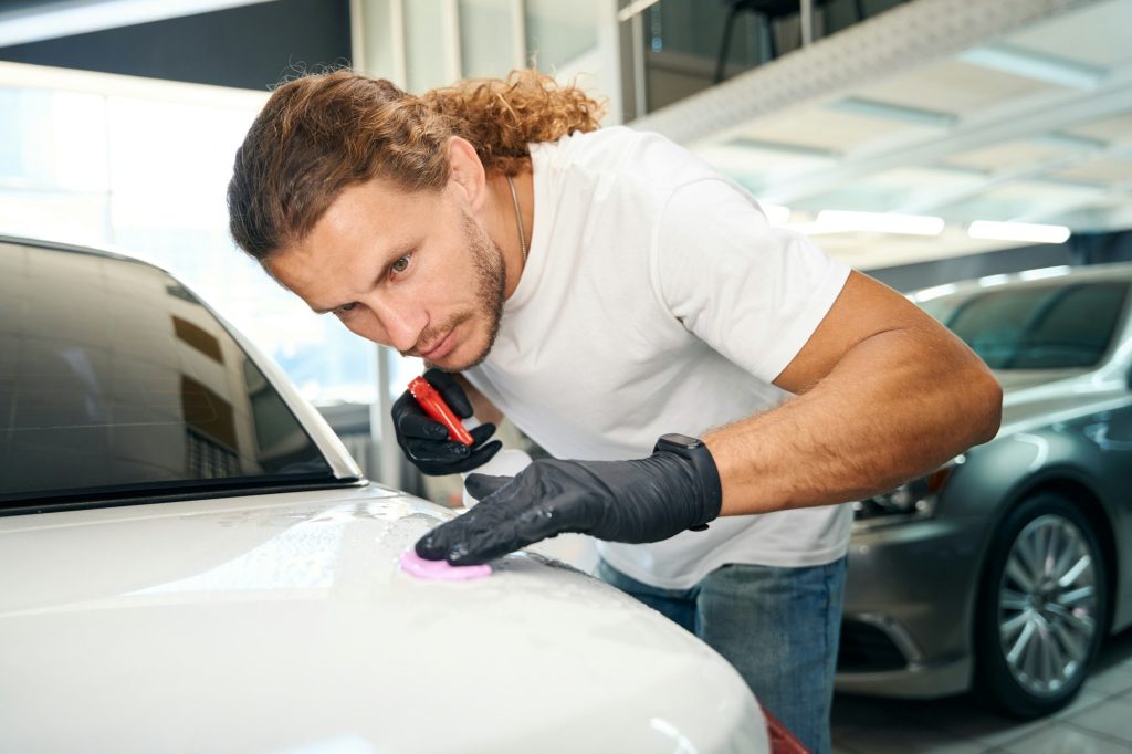 Man applies special clay to scratches on a car body